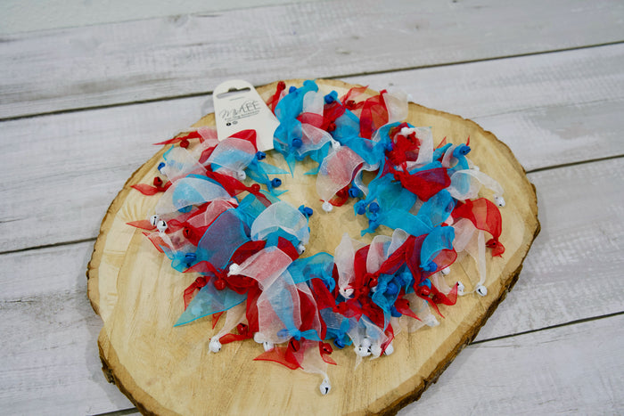 Red, white, and blue ribbons with bells for pet collars on a wooden board.|Rubans rouges, blancs et bleus avec des grelots pour colliers d'animaux, disposés sur une planche en bois.