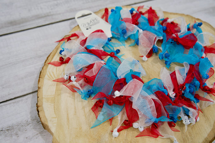 Decorative pet collar with red, white, and blue ribbons on a wooden surface.|Collier décoratif pour animal avec des rubans rouges, blancs et bleus, posé sur une surface en bois.