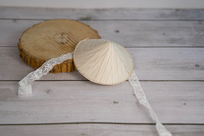 Traditional conical pet hat with a lace trim on a wooden surface.|Chapeau conique traditionnel pour animaux, bordé de dentelle, posé sur une surface en bois.