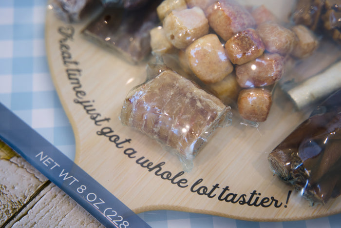 Assorted candies for dogs on a wooden board with text, on a checkered tablecloth.|Bonbons assortis pour chiens sur une planche en bois avec du texte, posée sur une nappe à carreaux.