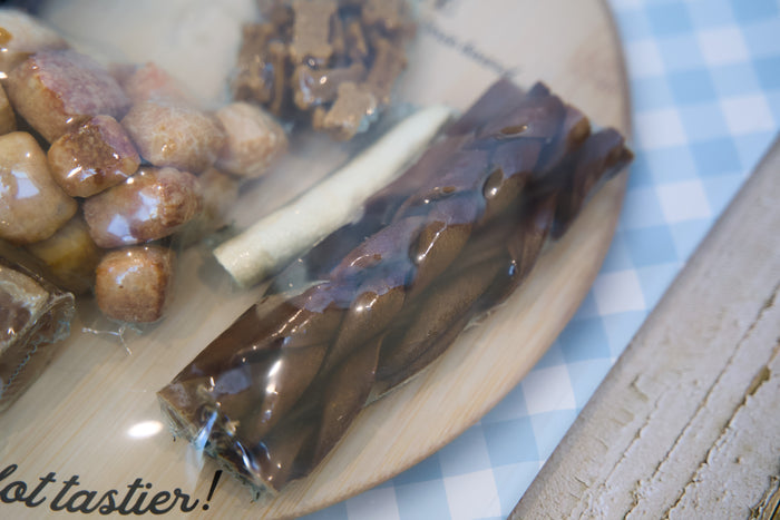 Close-up of a plate with dog chew treats items on a checkered tablecloth.|Gros plan d'une assiette contenant des friandises à mâcher pour chiens, posée sur une nappe à carreaux.