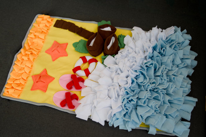 Pet snuffle mat designed to look like a beach scene, with fabric resembling sand, sea, and ocean waves.|Tapis de fouille pour chien imitant une scène de plage, avec des tissus représentant le sable, la mer et les vagues.