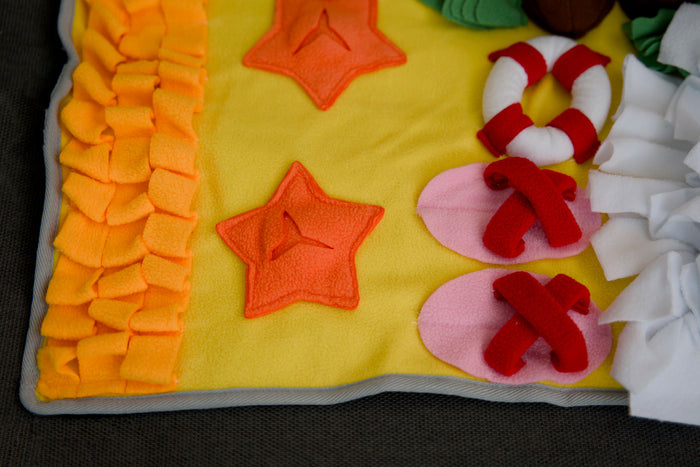 Close-up of a handmade snuffle mat with palm tree and seashell designs, crafted for pet enrichment.|Gros plan sur un tapis de fouille fait main avec des motifs de palmier et de coquillage, conçu pour la stimulation des animaux.