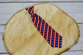 American flag patterned pet tie on a wooden surface.|Cravate pour animal à motifs de drapeau américain, posée sur une surface en bois.