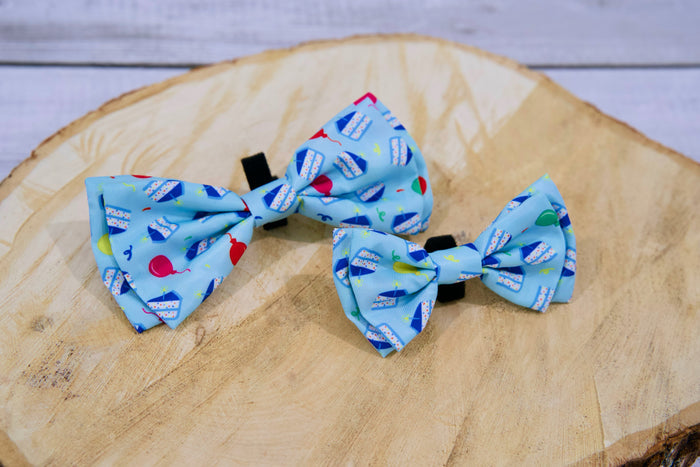 Two blue pet bow ties with colorful birthday patterns on a wooden surface.|Deux nœuds papillon bleus pour animaux, ornés de motifs d'anniversaire colorés, posés sur une surface en bois.
