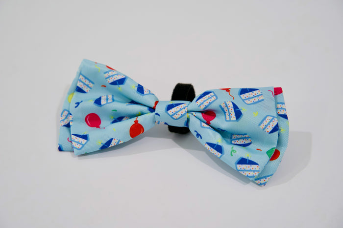 Blue bow tie with colorful balloon pattern on a white background.|Nœud papillon bleu à motif de ballons colorés sur fond blanc.