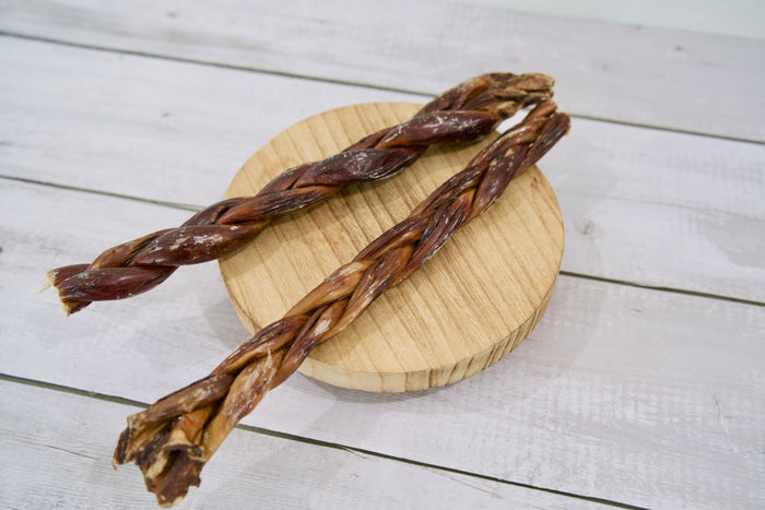 Two long braided dog treats with a dark reddish-brown color.|Deux longues friandises tressées pour chien, d'une couleur brun-rouge foncé.