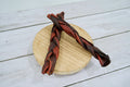 Two braided dog chew treats, one dark brown and one reddish-brown.|Deux friandises à mâcher tressées pour chien, l'une brun foncé et l'autre brun rougeâtre.