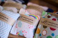 Colorful valerian bean bags for cats with labels on a wooden surface.|Des coussins colorés remplis de valériane pour chats, avec des étiquettes, posés sur une surface en bois.