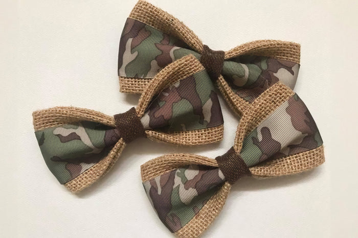 Three camouflage-patterned pet bow ties with brown accents on a white background.|Trois nœuds papillon pour animaux à motif camouflage, avec des touches de brun sur fond clair.