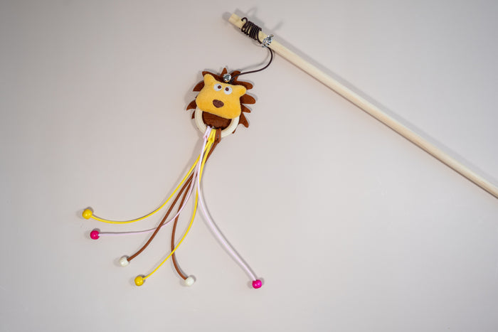 Cat teaser in the shape of a lion's head, leather rope and wooden beads. | Agace-chat en forme de tête de lion avec cordelettes en cuir et perles en bois.