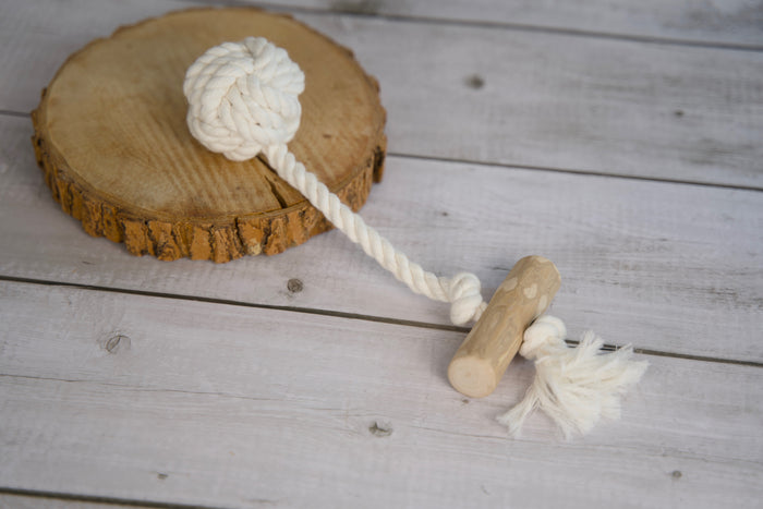 Rope dog toy and wooden handle on a wooden surface.|Jouet pour chien en corde et poignée en bois, posé sur une surface en bois.