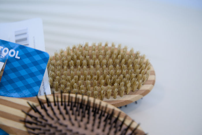 Two wooden pet brushes with bristle heads on a white surface.|Deux brosses pour animaux en bois avec des têtes à poils, posées sur une surface blanche.