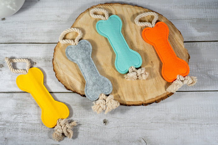 Felt bone dog toy with sturdy rope at the ends to encourage pulling. | Jouet pour chien en forme d'os en feutre avec une corde robuste aux extrémités pour encourager la traction.