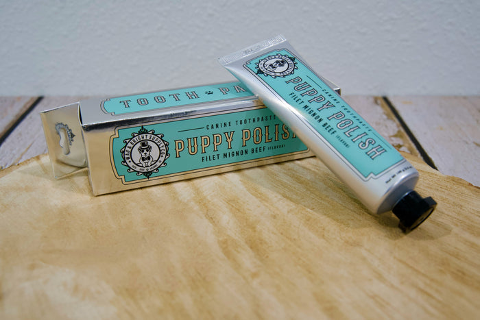 Puppy Polish filet mignon pet toothpaste tube and packaging on a wooden surface.|Tube et emballage de dentifrice pour animaux Puppy Polish (saveur filet mignon) posés sur une surface en bois.