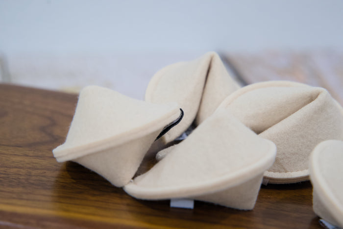 A close-up of fortune cookies felt pet toys arranged on a wooden surface.|Gros plan sur des jouets pour chat en feutrine en forme de biscuits de la chance, disposés sur une surface en bois.