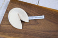 A fortune cookie cat toy with catnip and a tag that reads BLAME IT ON THE DOG.|Un jouet pour chat en forme de fortune cookie, contenant de l'herbe à chat et une étiquette portant l'inscription C'est la faute du chien.