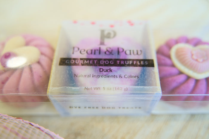 Pearl & Paw gourmet dog truffles packaging with pink truffles in the background.|Emballage des truffes pour chiens gastronomiques Pearl & Paw, avec des truffes roses en arrière-plan.