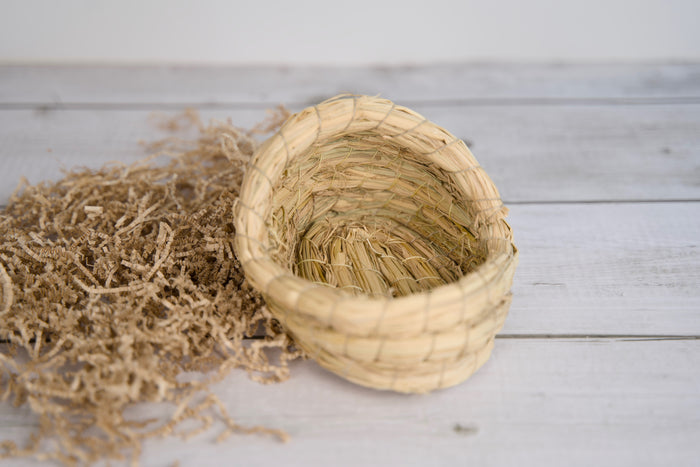 Woven straw basket for small pets on a wooden surface.|Panier en paille tressée pour petits animaux, posé sur une surface en bois.