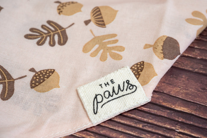 Close-up of The Paws logo on the soft pink cat bandana.|Gros plan sur le logo The Paws sur le bandana pour chat rose clair.