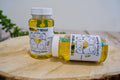Two bottles of 'Meow Mosa' cat wine bubbles on a wooden surface with a blurred background.|Deux bouteilles de vin pétillant pour chats « Mew & Moos » posées sur une surface en bois, avec un arrière-plan flou.