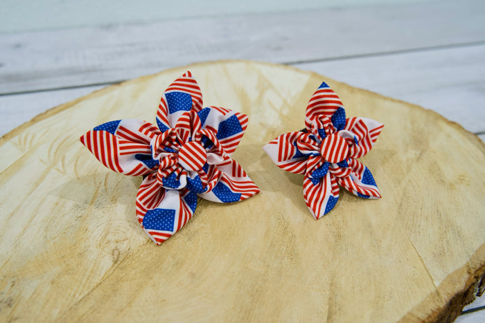 Two patriotic pet flower-shaped for pet collar on a wooden surface.|Deux accessoires patriotiques en forme de fleur pour collier de chien ou chat, posés sur une surface en bois.