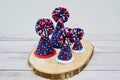 Red, white, and blue pet party hats and pom-poms on a wooden surface.|Chapeaux de fête et pompons aux couleurs rouge, blanc et bleu pour animaux, disposés sur une surface en bois.