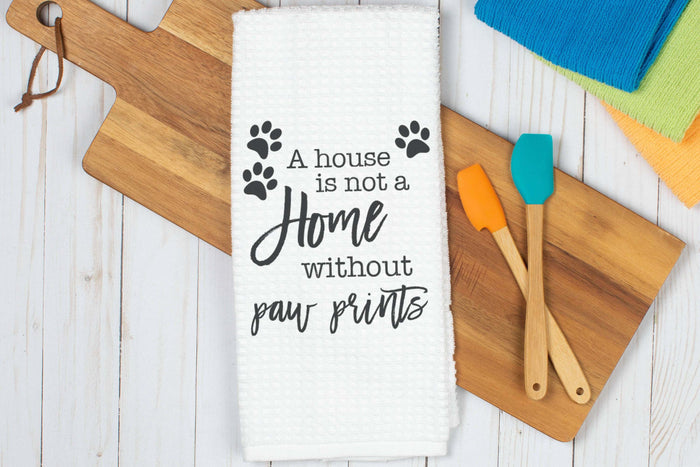 Pet-themed kitchen white towel with text and paw prints on a wooden cutting board.|Torchon de cuisine blanc sur le thème des animaux, orné de texte et d'empreintes de pattes, posé sur une planche à découper en bois.