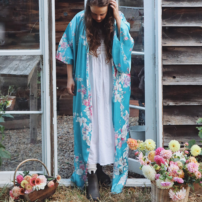 Woman wearing a floral kimono standing outdoors with flowers and a wooden door in the background