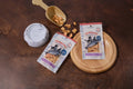 Two packages of Salmon Poke dog and cat treats are displayed on a dark brown textured surface.|Deux paquets de friandises « Salmon Poke » pour chiens et chats sont présentés sur une surface texturée brun foncé.
