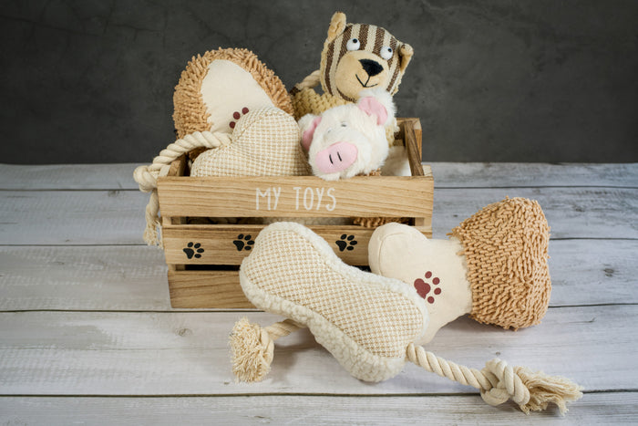 Wooden basket with neutral colored plush and rope toys for dogs. | Panier en bois avec jouets en peluche pour chiens.