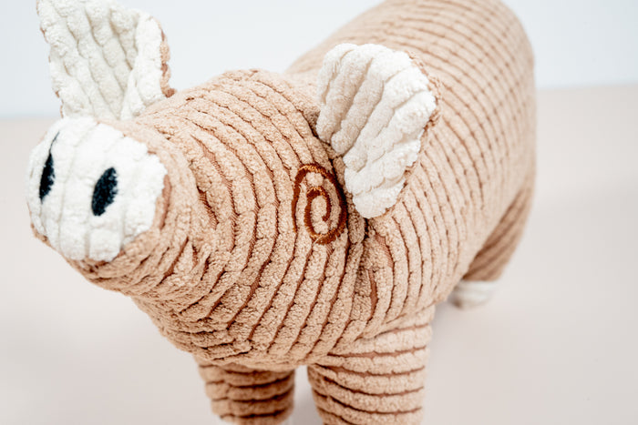 Close-up view of brown pig plush dog toy. | Vue rapprochée du jouet pour chien en peluche cochon marron.