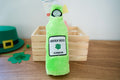 Green plush bottle dog toy with Green Beer Superior label on a wooden surface.|Jouet pour chien en peluche verte en forme de bouteille avec une étiquette Green Beer Superior sur une surface en bois.