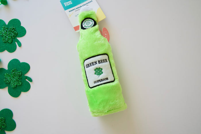 Green plush bottle toy for dogs labeled Green Beer with shamrock decorations on a white background.|Jouet en peluche verte en forme de bouteille pour chiens, étiqueté Bière Verte avec des décorations de trèfle sur fond blanc.