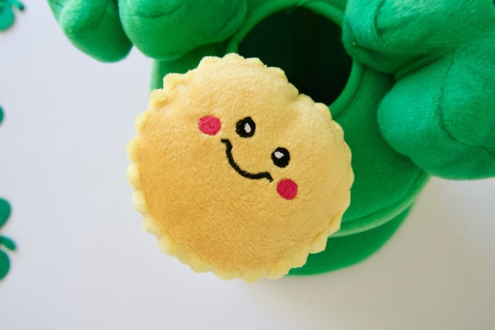 Plush dog toy with a smiley face design held by green gloves on a white background.|Peluche pour chien avec un visage souriant, tenue par des gants verts sur fond blanc.