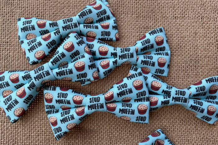 Multiple dog and cats bow ties with stud muffin pattern on a textured fabric background.|Lot de nœuds papillon pour chiens et chats, à motif Stud Muffin sur fond en tissu texturé.