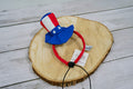Colorful pet headband with American flag design on a wooden surface.|Bandeau coloré pour animal avec un motif de drapeau américain, posé sur une surface en bois.