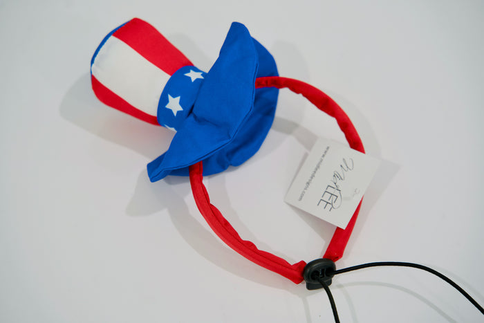 Red, white, and blue dog headband with a bow on a white background.|Serre-tête pour chien rouge, blanc et bleu avec un nœud, sur fond blanc.