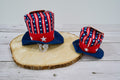 Two dog hats with American flag design on a wooden surface.|Deux chapeaux pour chien à motif de drapeau américain sur une surface en bois.
