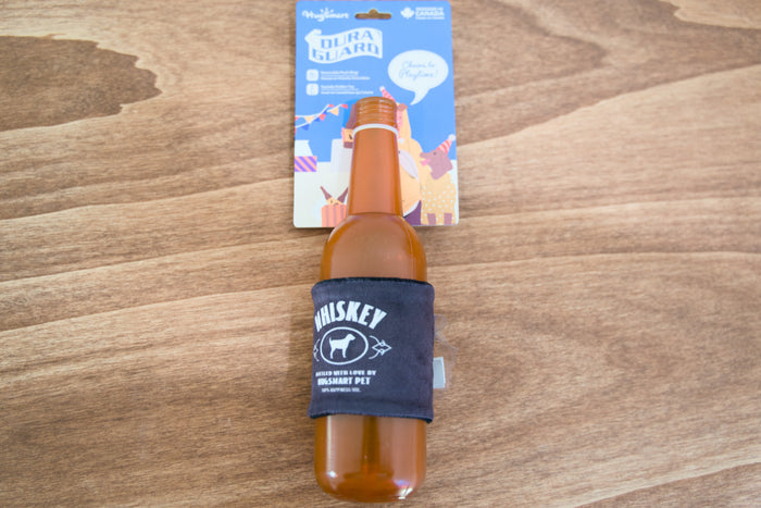 Bottle of whiskey for dogs with a blue sleeve on a wooden surface, with a product packaging in the background.|Une bouteille de whisky pour chiens avec un étui bleu posée sur une surface en bois, avec l'emballage du produit en arrière-plan.