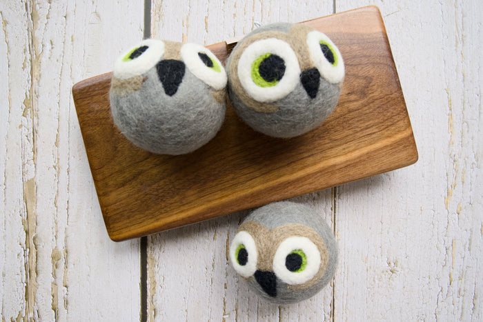 Three gray felt owl dog toys arranged on a wooden board.|Trois jouets pour chiens en forme de hibou, en feutrine grise, disposés sur une planche en bois.