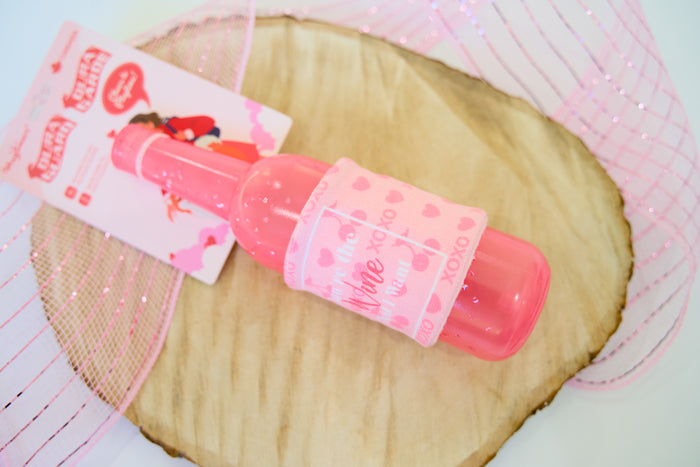 Pink wine bottle for dogs on a wooden surface.|Une bouteille de vin rose pour chiens posée sur une surface en bois.