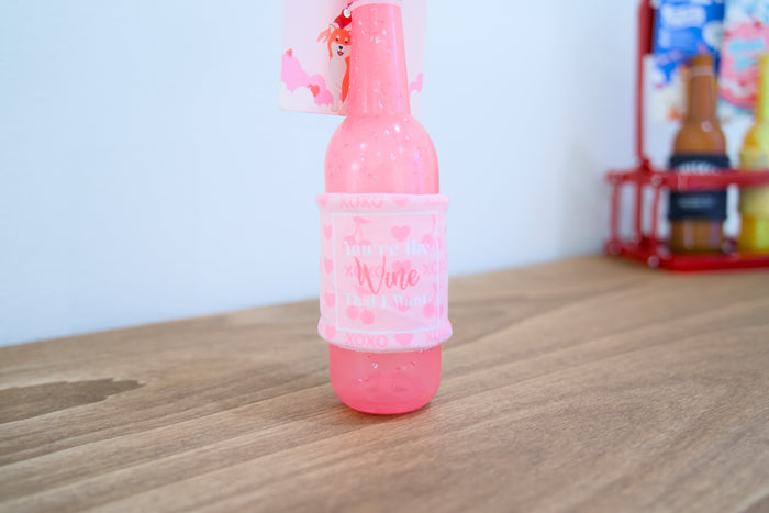 Pink bottle valentines dog toy on a wooden surface.|Jouet pour chien en forme de bouteille rose sur une surface en bois, pour la Saint-Valentin.